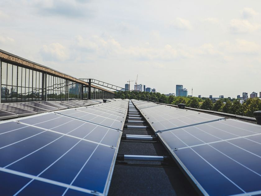 Two long rows of solar panels on a flat roof, leading towards a city skyline